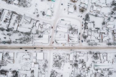 Kışın küçük bir köyün havadan görünüşü. Kırsal yol karla kaplı evlerin arasından geçiyor. Kış manzarası