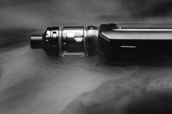 Electronic cigarette in smoke on a black background, smoking nicotine through an electronic cigarette, vaping on a black background
