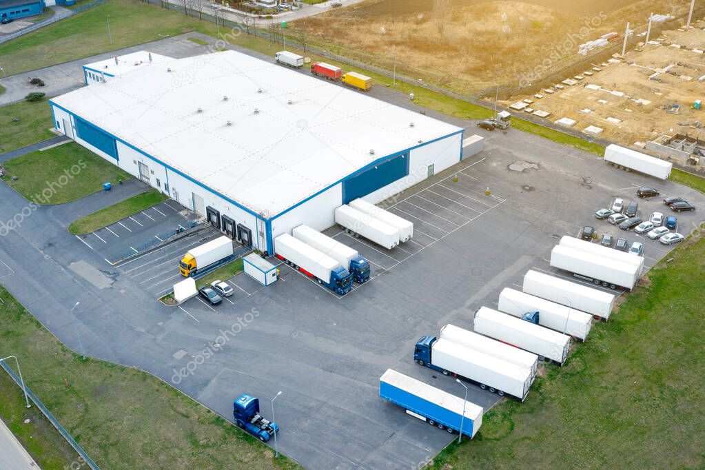 Aerial view of a logistics park with a warehouse, trucks with trailers stand in a parking lot and wait for unloading and loading