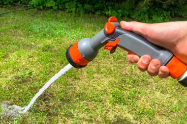 Bahçıvanın eli bir hortumu spreyle tutar ve çimleri sular.