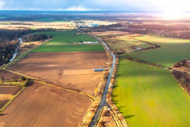 Yeşil bir tarlanın üzerinde uçuyor, tarlaların ve yolların yüksekliğinden bir manzara.