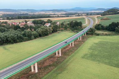 Top view of a long bridge passing through green fields