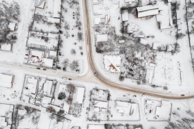 Kışın küçük bir köyün havadan görünüşü. Kırsal yol karla kaplı evlerin arasından geçiyor. Kış manzarası