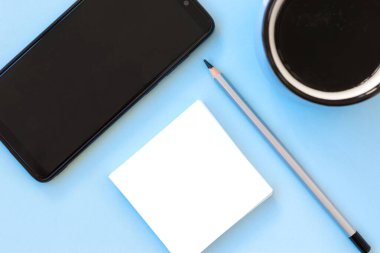 Akıllı telefon, beyaz kağıt not, bir fincan kahve ve açık mavi arka planda bir kalem ile düz yatıyordu. Model yap, boşluğu kopyala.