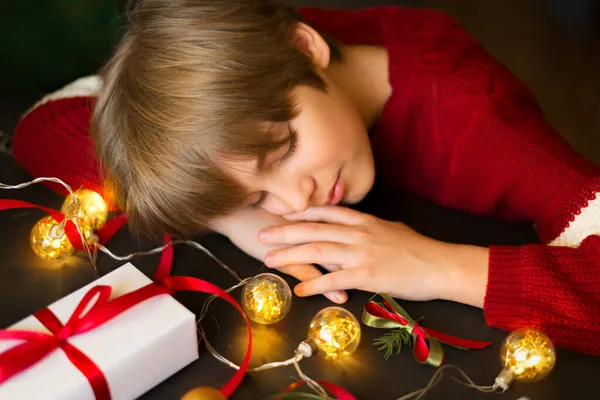 Çocuk bir hediye ve çelengin yanında uyuyor. Noel Baba 'yı, Noel' i ve yeni yılı bekliyorum.