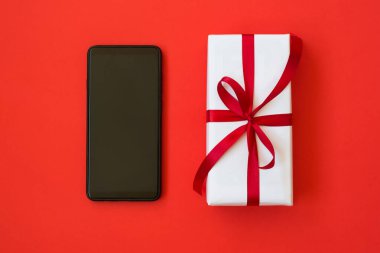 Beyaz hediye kutusu ve kırmızı arka planda bir akıllı telefon.