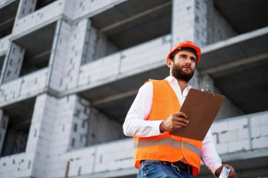 İnşaat alanında çalışan genç mühendis elinde panoyla duruyor.