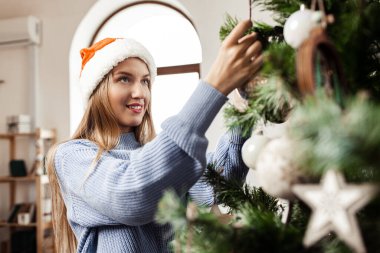Mavi kazaklı genç sarışın kadın Noel ağacını süslüyor.