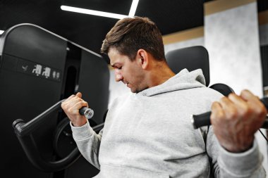 Genç, formda vücut geliştirici adam spor salonunda makineyle antrenman yapıyor.