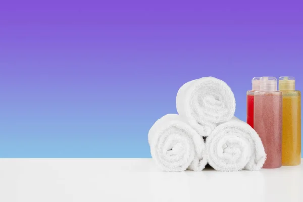 Pilha de toalhas, garrafas com shampoo na mesa branca — Fotografia de Stock