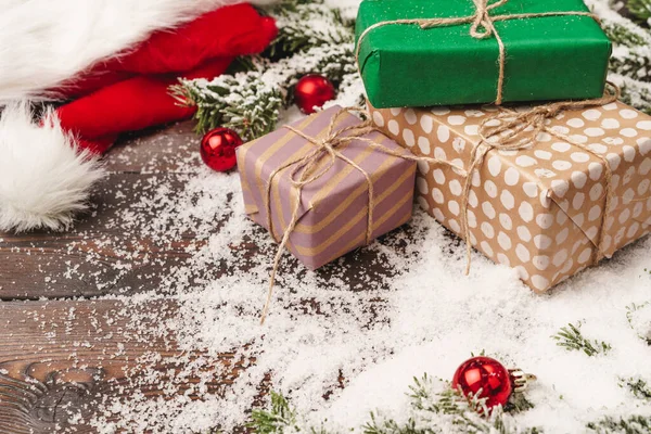 Regalos sobre fondo de madera con ramas de abeto y adornos rojos en polvo con nieve —  Fotos de Stock