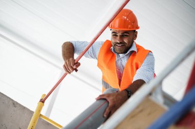 İnşaat alanındaki iskeleye tırmanan genç yakışıklı inşaatçı.