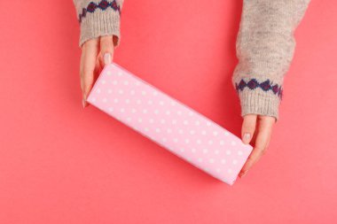 Kadının ellerinin pembe arka planda hediye kutusunu tutuşu.