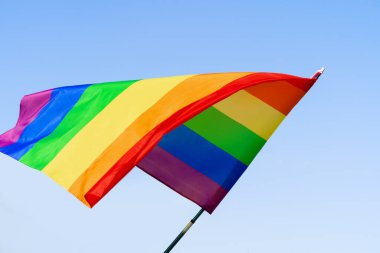 Açık mavi gökyüzünde rüzgarda sallanan eşcinsel gökkuşağı bayrağı