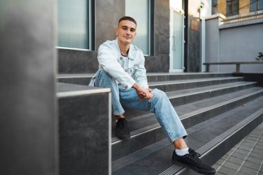 Sokakta tek başına merdivenlerde oturan sıradan bir genç.