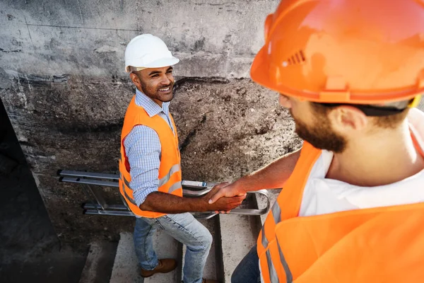 Två män ingenjörer i arbetskläder skakar hand mot byggarbetsplatsen. — Stockfoto