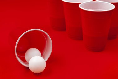 Bardaklar ve plastik top kırmızı arka planda. Bira pong oyunu
