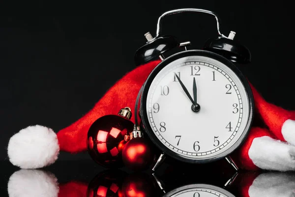 Black vintage alarm clock with christmas baubles and decor on dark black background. Christmas eve concept — Stock Photo, Image