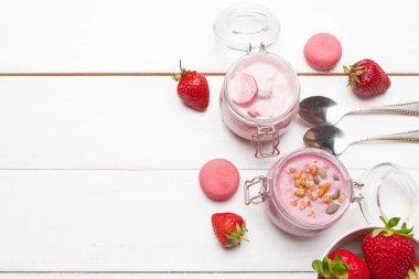 Beyaz ahşap arka plan üst görünümünde yoğurt, granola ve çilek ile sağlıklı kahvaltı