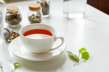 Kuru çay kavanozuyla beyaz masada bir fincan sıcak siyah çay.