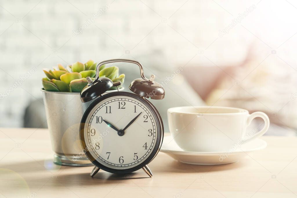 Classic vintage alarm clock and coffee cup on wooden background