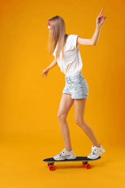 Teenager-Mädchen steht und posiert auf Skateboard vor farbigem Hintergrund — Stockfoto