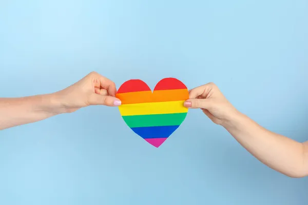 Amor gay. Mano humana sosteniendo un corazón de papel arco iris — Foto de Stock