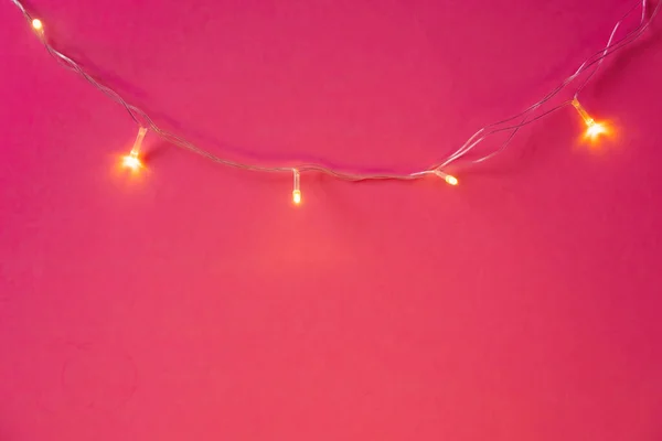 Luzes de guirlanda iluminadas no fundo rosa brilhante — Fotografia de Stock