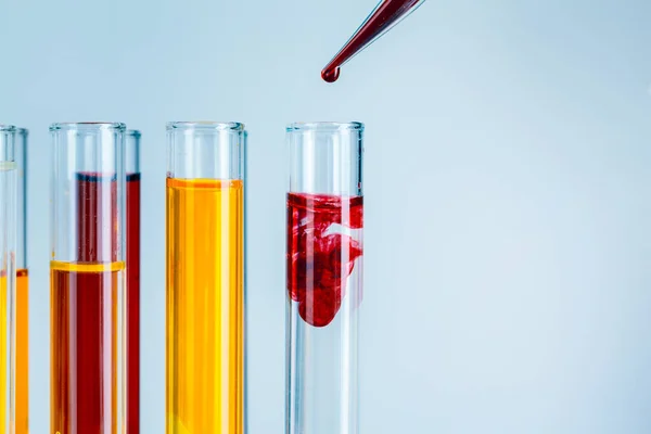 Εργαστηριακοί δοκιμαστικούς σωλήνες με κόκκινα και κίτρινα υγρά σε ανοιχτό γαλάζιο φόντο — Φωτογραφία Αρχείου