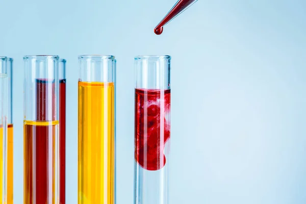 Εργαστηριακοί δοκιμαστικούς σωλήνες με κόκκινα και κίτρινα υγρά σε ανοιχτό γαλάζιο φόντο — Φωτογραφία Αρχείου