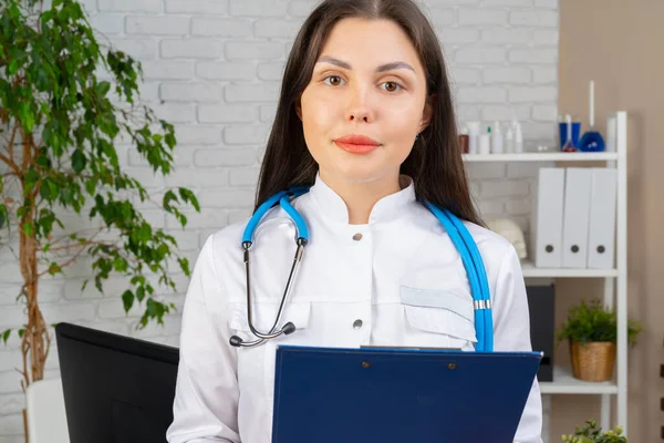 Ung brunett kvinna läkare stående med urklipp på sitt kontor — Stockfoto