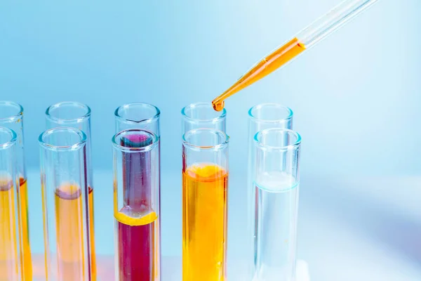Tubos de ensaio de laboratório com líquidos vermelhos e amarelos sobre fundo azul claro — Fotografia de Stock