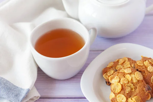 Tasse Tee mit Keksen über fliederfarbenem Holzhintergrund Stockbild