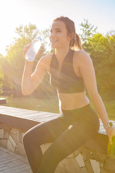 Young beautiful woman drinking water during morning jogging in the park — Stock Photo, Image