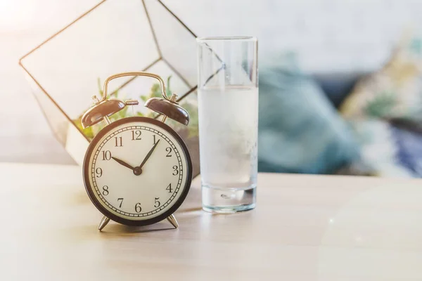 飲料水健康の概念。テーブルの上の目覚まし時計と水のガラス — ストック写真
