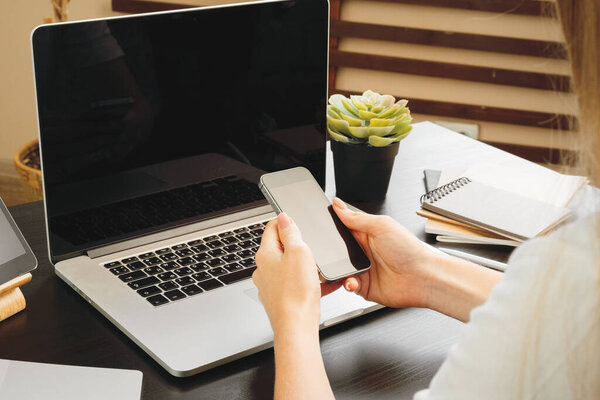 Smartphone with black screen in female hands. Computer, keyboard and office supplies on a background