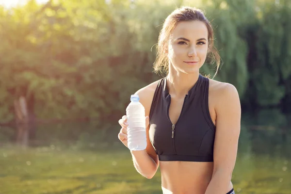 Young beautiful woman drinking water during morning jogging in the park — Stock Photo, Image