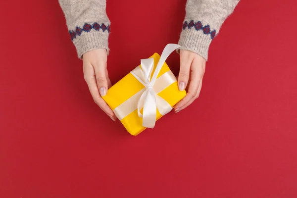 Mains féminines avec cadeau de Noël sur fond rouge, vue du dessus, espace de copie — Photo