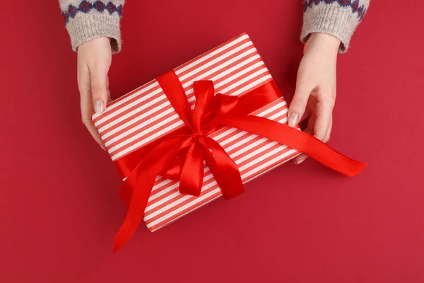 Mains féminines avec cadeau de Noël sur fond rouge, vue du dessus, espace de copie — Photo