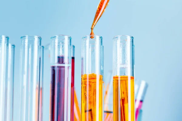 Tubes à essai de laboratoire avec liquides rouges et jaunes sur fond bleu clair — Photo