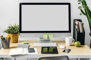 Ofis masasında malzemelerle birlikte beyaz ekranlı bilgisayar monitörü