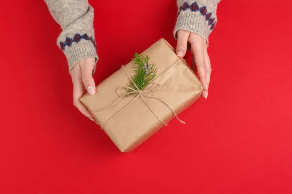 Mains féminines avec cadeau de Noël sur fond rouge, vue du dessus, espace de copie — Photo