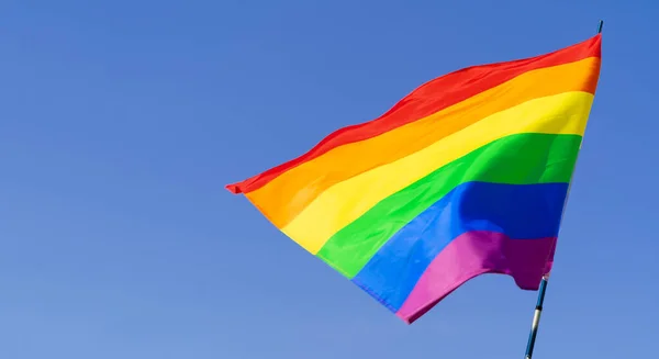 Açık mavi gökyüzünde rüzgarda sallanan eşcinsel gökkuşağı bayrağı — Stok fotoğraf