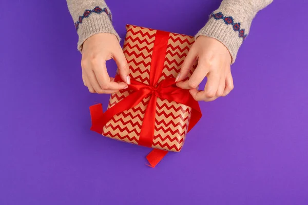 Les mains féminines tenant cadeau enveloppé sur fond violet — Photo