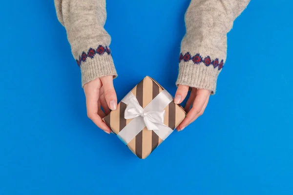 Kleine geschenkdoos in vrouwelijke handen op blauwe achtergrond, uitzicht van boven — Stockfoto