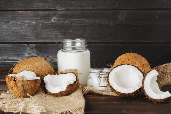 Coco quebrado e leite de coco em fundo de madeira preta — Fotografia de Stock