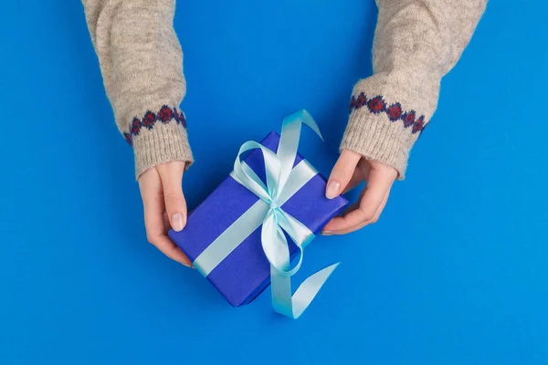 Μικρό κουτί δώρου σε γυναικεία χέρια σε μπλε φόντο, θέα από ψηλά — Φωτογραφία Αρχείου