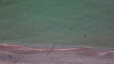 Güneşin doğuşunda, kumsalda yürüyen adamla birlikte güzel bir sahil ve deniz suyunun insansız hava aracı görüntüsü.