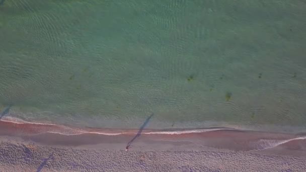 Veduta aerea drone di una bella spiaggia e acqua di mare al sorgere del sole con l'uomo a piedi sulla spiaggia — Video Stock