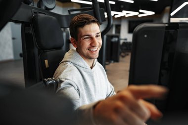 Genç, formda vücut geliştirici adam spor salonunda makineyle antrenman yapıyor.